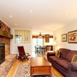 A cozy living room with a brick fireplace, comfortable sofa, and a view of the dining area.