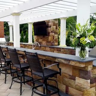 A stylish outdoor bar area featuring a stone countertop, high chairs, and a beautiful floral arrangement.