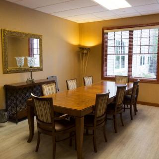 A well-furnished conference room with a large meeting table and chairs, featuring a mirror and window.
