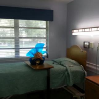 An empty hospital room with a single bed and flowers on the bedside table.