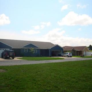 A suburban house with a green lawn and cars parked in the driveway.