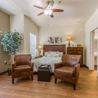 A cozy bedroom with two leather chairs, a bed, and wooden flooring.