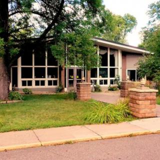 A modern building with large windows surrounded by trees and a neatly maintained landscape.
