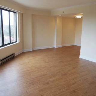 A vacant apartment room with wood flooring and large windows allowing natural light.