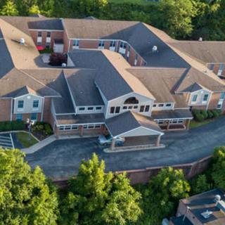 Aerial view of a large building surrounded by lush greenery and a winding driveway.