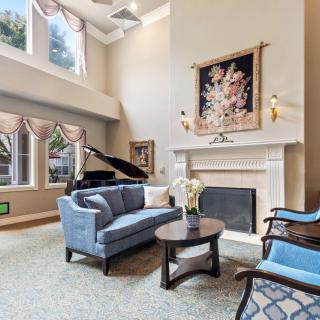 A spacious living room featuring a grand piano, elegant furniture, and a warm fireplace with artwork above.