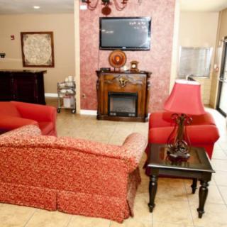 A cozy living room with red upholstered furniture, a TV mounted above a decorative fireplace, and elegant decor.