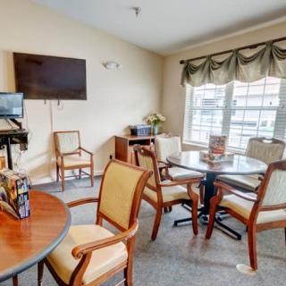 A cozy seating area with tables, chairs, a television, and a large window with curtains.