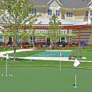 An outdoor area featuring a putting green with flags, surrounded by lush landscaping and a residential building.