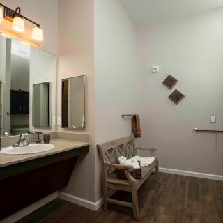 A modern bathroom with a large mirror, wooden bench, and stylish lighting.