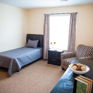 A cozy, well-lit bedroom featuring a single bed, decorative chair, and natural light from the window.