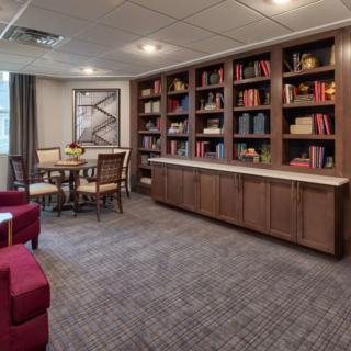 A cozy library room with bookshelves, a table and chairs, and art on the wall.