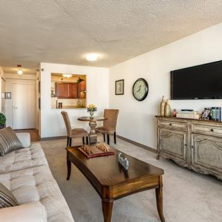 A modern living room with a comfortable sofa, wooden coffee table, and a wall-mounted television, adjacent to a small dining area.