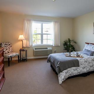 A cozy bedroom with a bed, window, chair, lamp, and dresser.