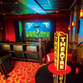 A cozy theater interior featuring red seating, a vibrant screen display, and a warm ambiance.