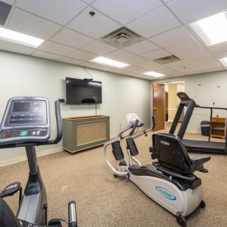 A small gym with exercise equipment including a treadmill and stationary bike, along with a television on the wall.