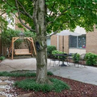A peaceful garden with a tree, swing, and patio seating area.