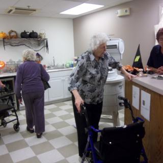 Elderly individuals interacting in a kitchen setting with assistance from staff.