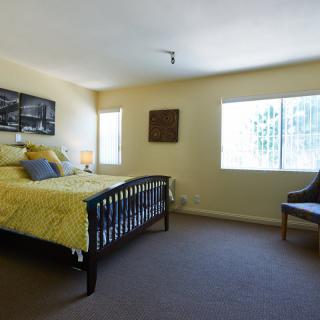 A cozy bedroom with a bed, chair, and windows allowing natural light.