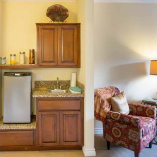 A cozy living space featuring a kitchenette with cabinets, a sink, and a mini fridge adjacent to an armchair and lamp.