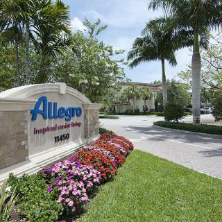 Entrance sign for Allegro, featuring landscaping and flowers with palm trees in the background.