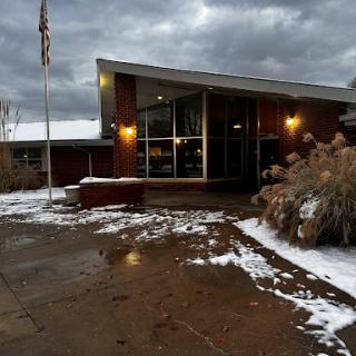 A modern building entrance surrounded by snow, set against a backdrop of cloudy skies.
