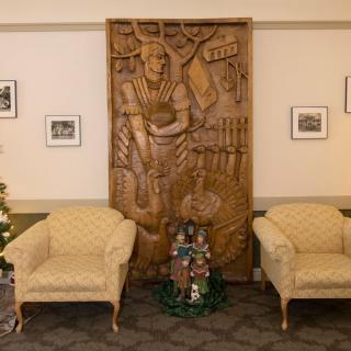 A cozy room featuring a detailed wood carving, flanked by two armchairs with framed photographs on the wall.