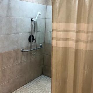 A tiled shower with a curtain and grab bar for accessibility.