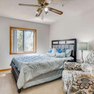 A cozy bedroom featuring a double bed, a patterned armchair, a ceiling fan, and a window providing natural light.