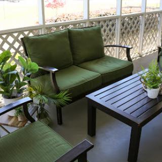 A cozy outdoor seating area featuring a green couch, chairs, and a table surrounded by plants.