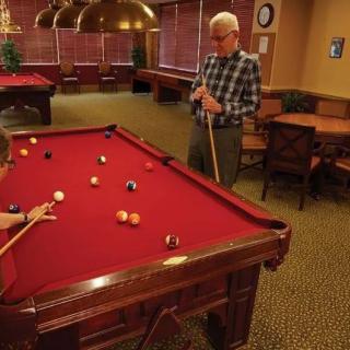 Two people playing billiards in a game room with a red pool table.