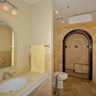 A well-lit bathroom featuring a sink with a mirror, a yellow towel, a toilet, and an arched tiled shower area.