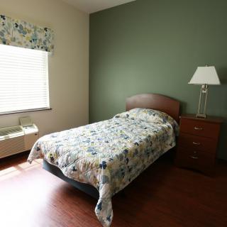 A simple bedroom with a single bed, nightstand, and lamp.
