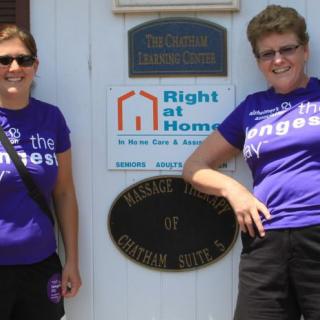 Two women standing in front of building signs, wearing purple t-shirts.