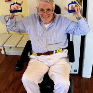 An elderly man in a wheelchair exercising with hand grips indoors.