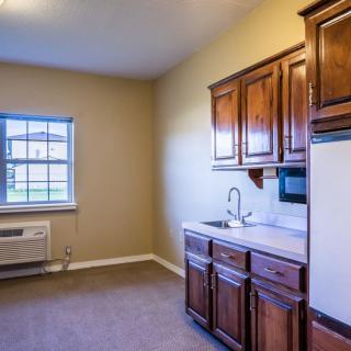 A compact kitchen interior with wooden cabinets, a small sink, and an air conditioner by the window.