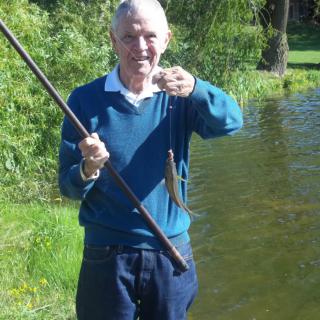 A man holding a fishing rod and displaying his catch by a lake.
