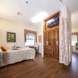 A modern hospital room designed for patient comfort, featuring a single bed, wooden flooring, and a television.
