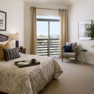 A cozy bedroom with a bed, chair, and a large window overlooking greenery.