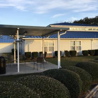 A serene view of a building with a patio area, surrounded by neatly trimmed bushes under a clear evening sky.