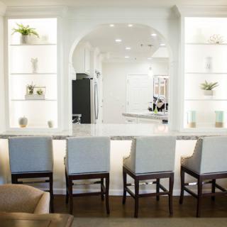 A modern kitchen interior with bar stools and decorative shelves.