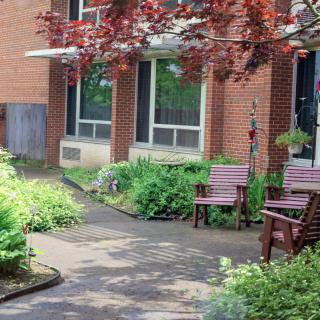 A peaceful garden setting with benches and lush greenery beside a brick building.