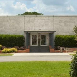 A concrete building entrance surrounded by neatly trimmed bushes under a cloudy sky.