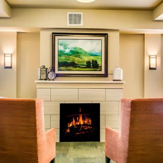 A cozy living room with a lit fireplace, flanked by two comfortable chairs and adorned with artwork above.