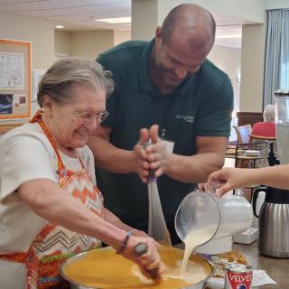 A man and an elderly woman enjoying a baking activity together in a kitchen.