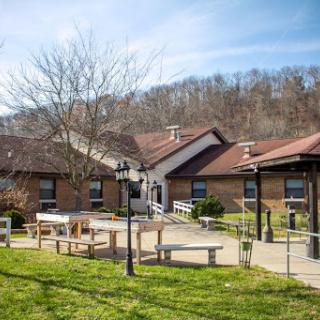 A serene outdoor setting featuring a residential building surrounded by greenery and picnic tables, ideal for relaxation and recreation.