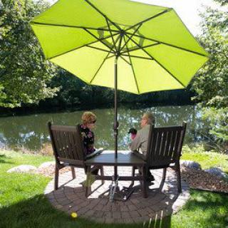 Two people sitting under a green umbrella by a lake, enjoying the outdoor scenery.