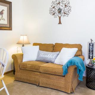 A cozy living room setup with a comfortable couch, adorned with throw pillows and a soft blanket. A stylish wall art piece and a lamp complete the inviting atmosphere.
