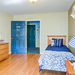 A neatly arranged bedroom featuring a single bed with blue bedding, wooden flooring, and a classic dresser.