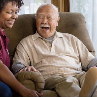 An elderly man sitting and smiling with a caregiver by his side.